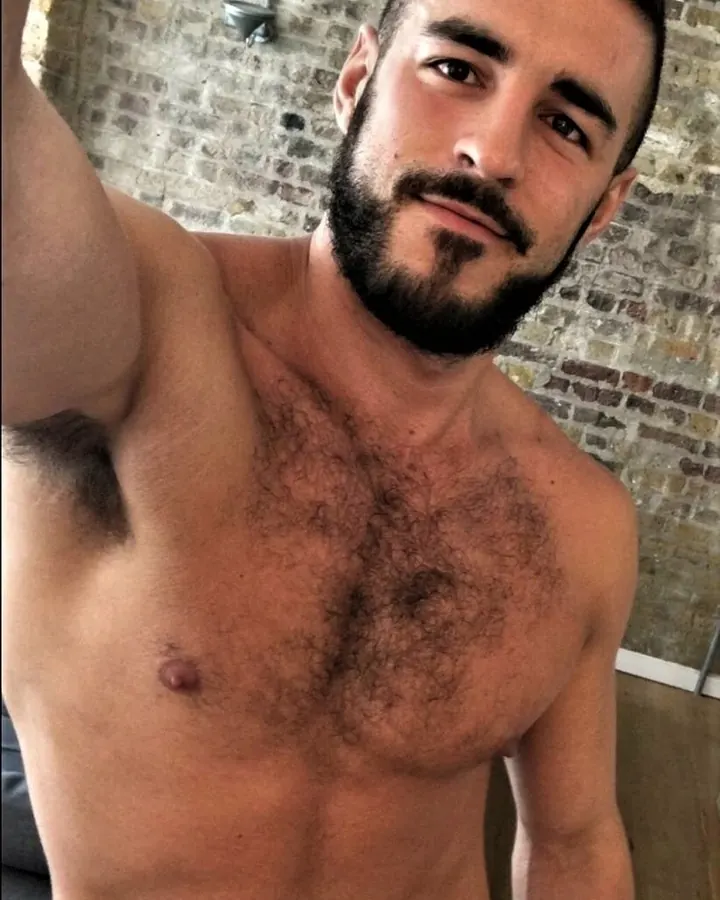 Homme torse nu, portant un short à motifs, posant dans un cadre sombre
