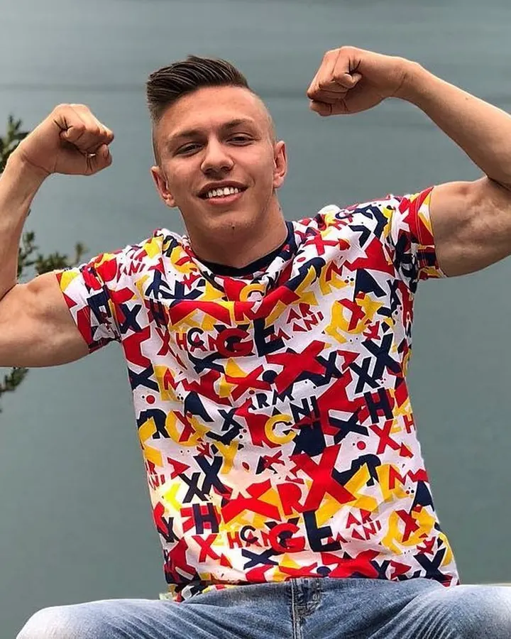 Homme souriant, portant un t-shirt coloré, faisant le geste de flexion des bras