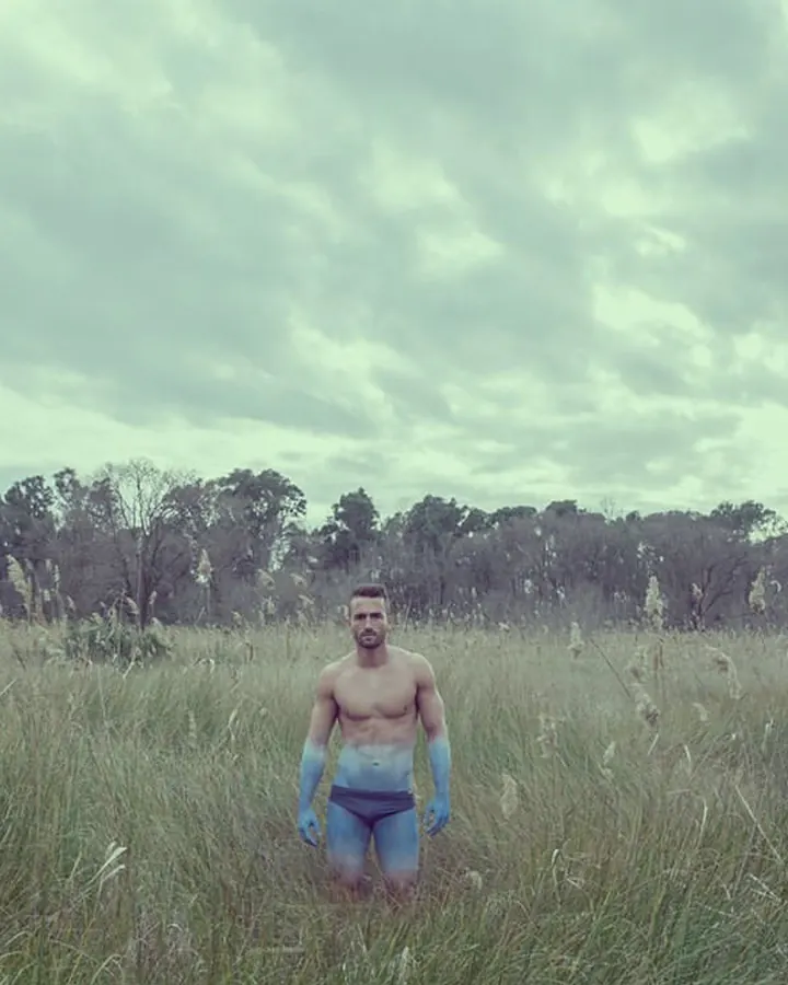 Homme torse nu, en short de plage, debout sur une plage, regardant vers la mer.