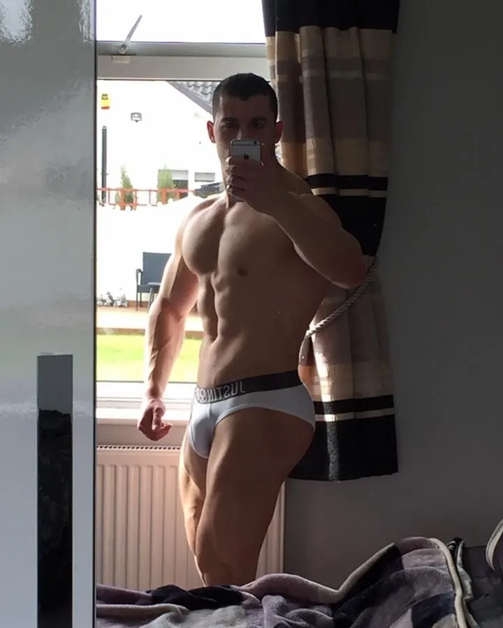 Homme torse nu en sous-vêtement blanc, prenant un selfie devant une fenêtre