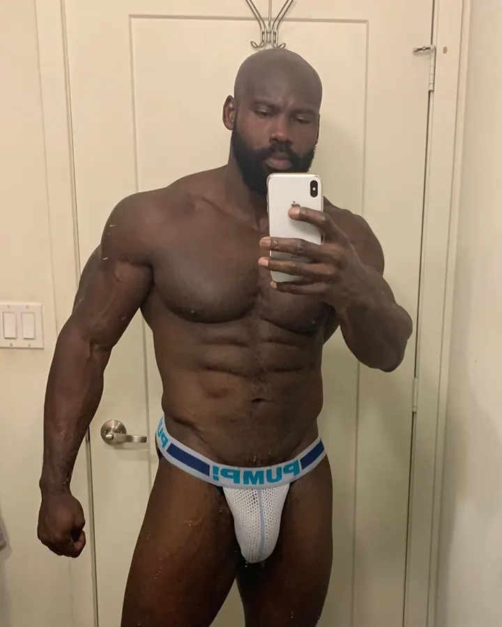 Homme torse nu, prenant un selfie dans un miroir, portant un t-shirt noir, regardant vers la caméra