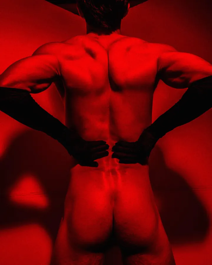 Homme torse nu, cheveux châtains, regardant directement l'objectif, dans un cadre sombre