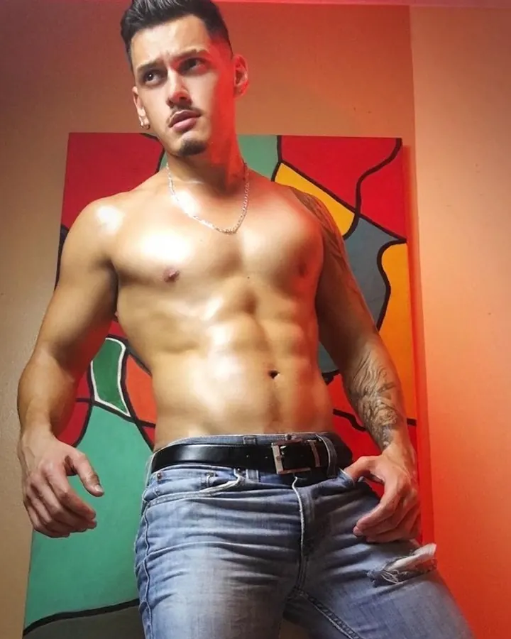 Homme torse nu, cheveux bruns, regardant directement l'objectif, dans un cadre sombre
